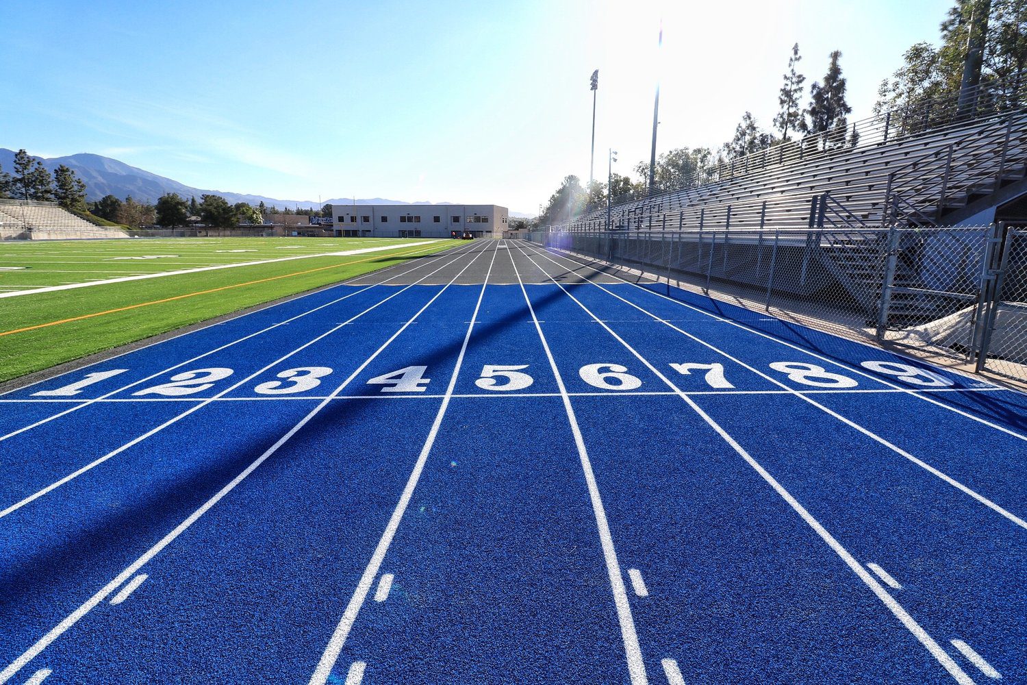 Blue running track lanes numbered 2 to 8 with a sports field in the background.