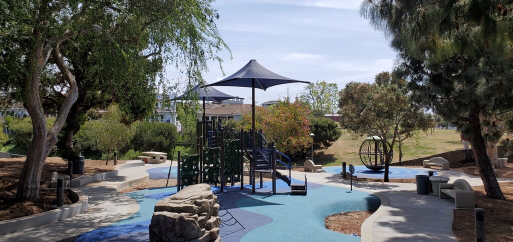 Children playing on a colorful playground under a large shade umbrella.