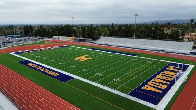 View of a clean, empty football field with track and stands under a cloudy sky.