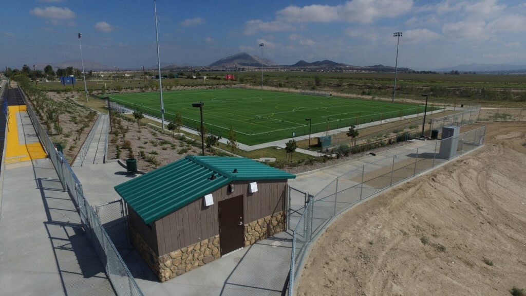 A green soccer field with surrounding fencing and a small building.