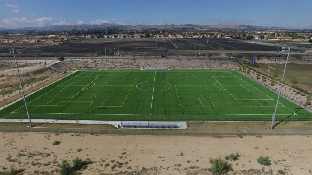 A green soccer field with surrounding barren land and distant hills.