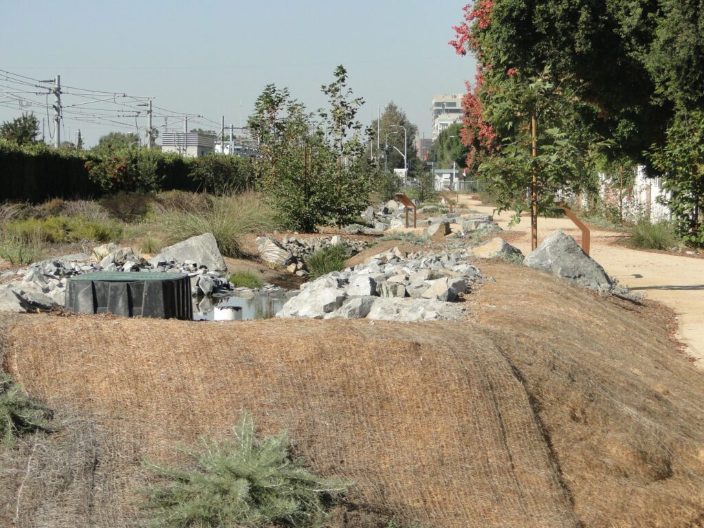 Dry riverbed with scattered rocks and sparse vegetation.