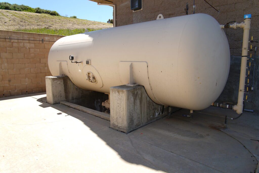 Large white industrial storage tank mounted on concrete blocks outdoors.