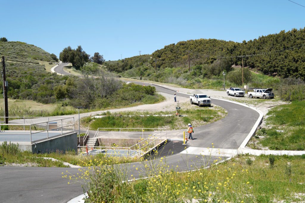 Two cars driving on a winding road through a green, hilly area.