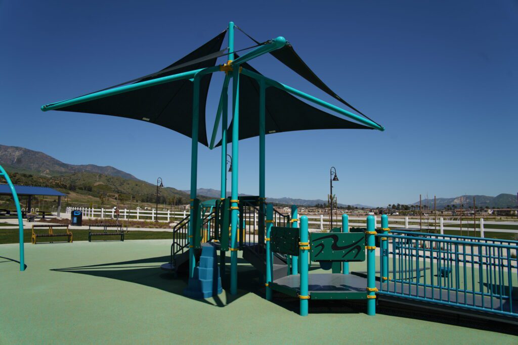 A shaded playground area with blue-green structures under a clear sky.