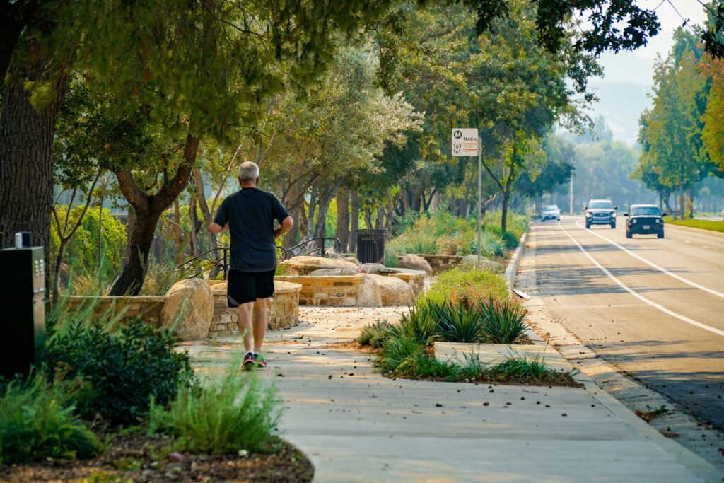A man jogging on a sunny sidewalk lined with trees and plants.