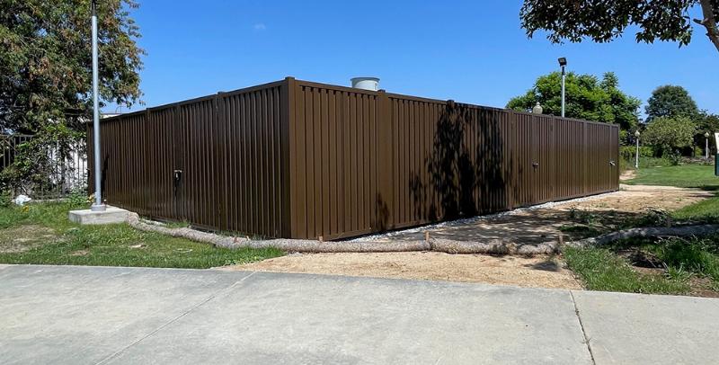 A tall brown metal fence enclosing a yard under clear blue sky.