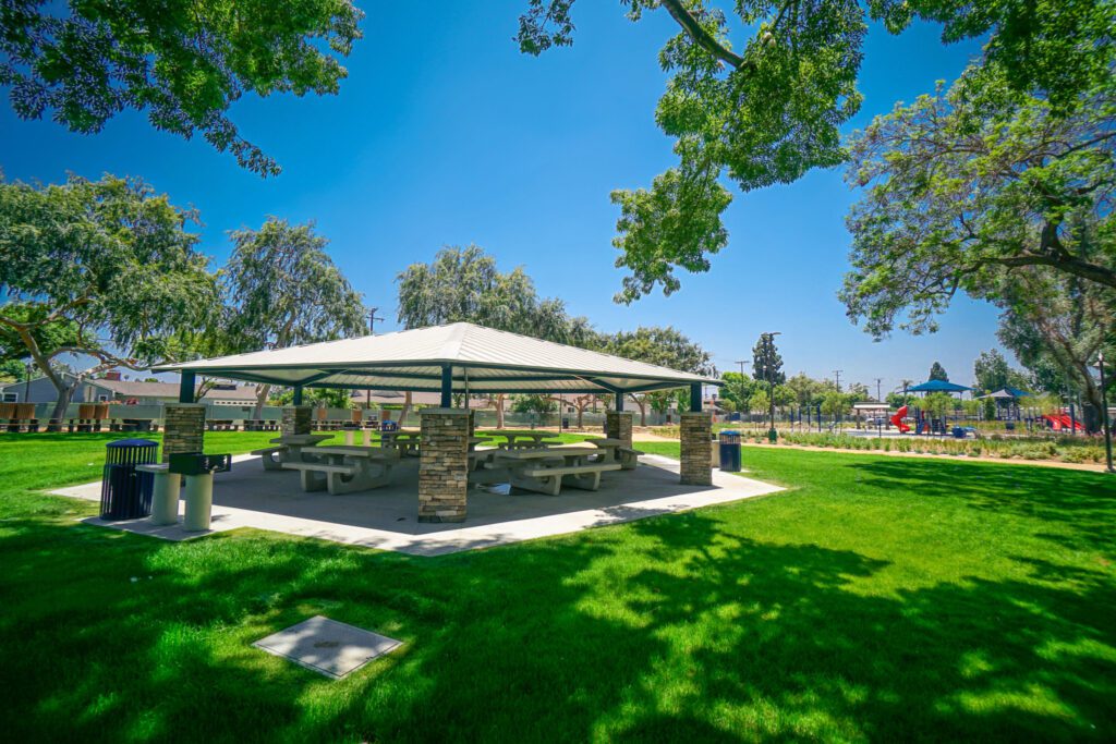 Modern outdoor pavilion with picnic tables in a sunny green park.