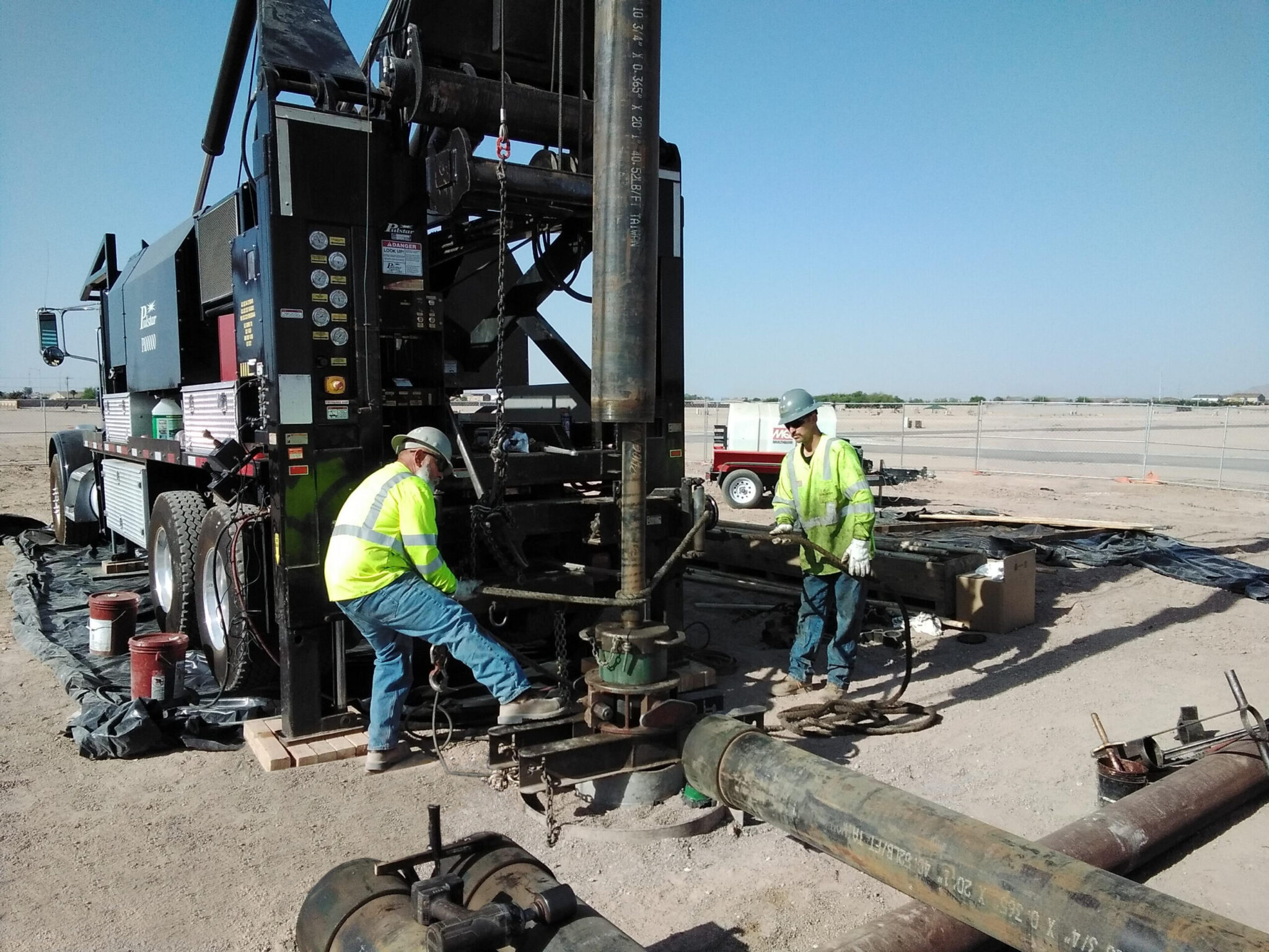 Two workers operate heavy machinery on a construction site under clear skies.