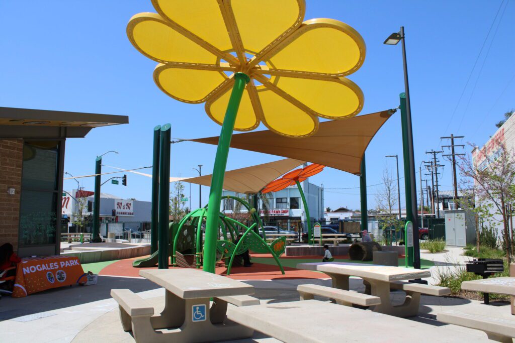 Colorful playground with a giant yellow flower shade and seating area under clear blue sky.