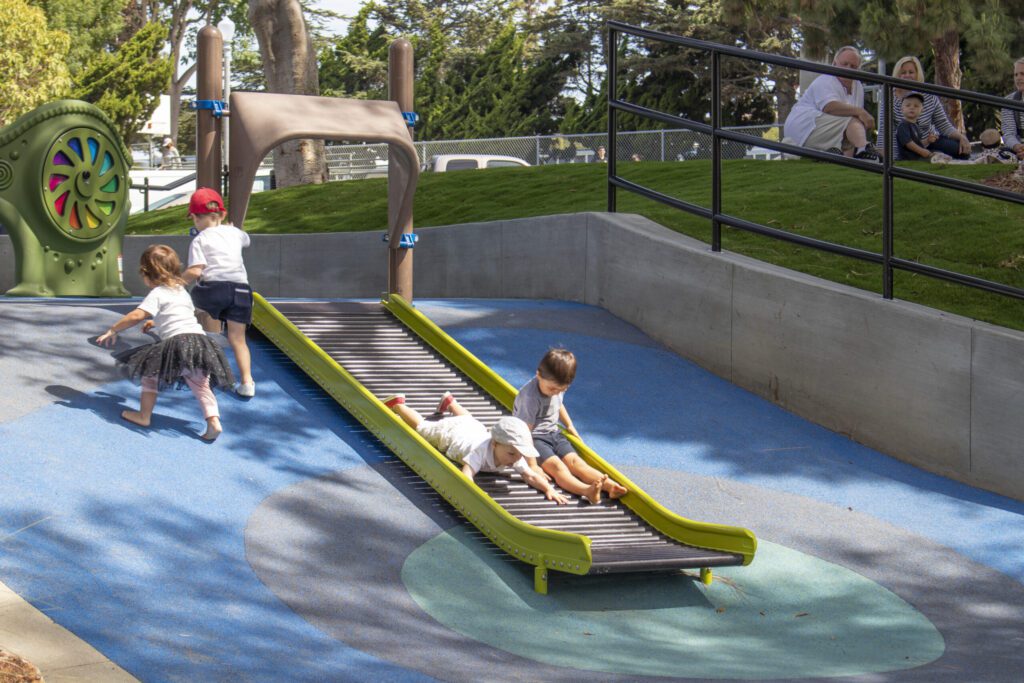 Two children playing on a slide at a park.