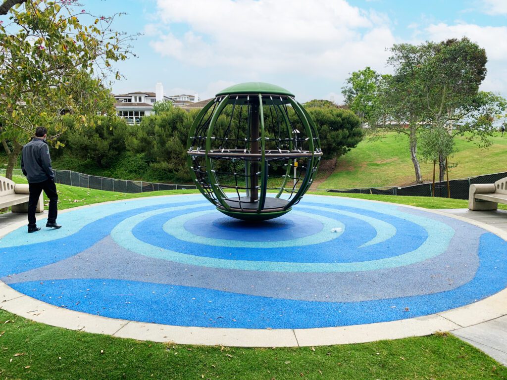 A metallic globe sculpture in a park surrounded by blue circular patterns.