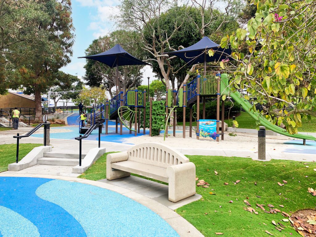 Modern playground with slides, swings, and benches in a park.