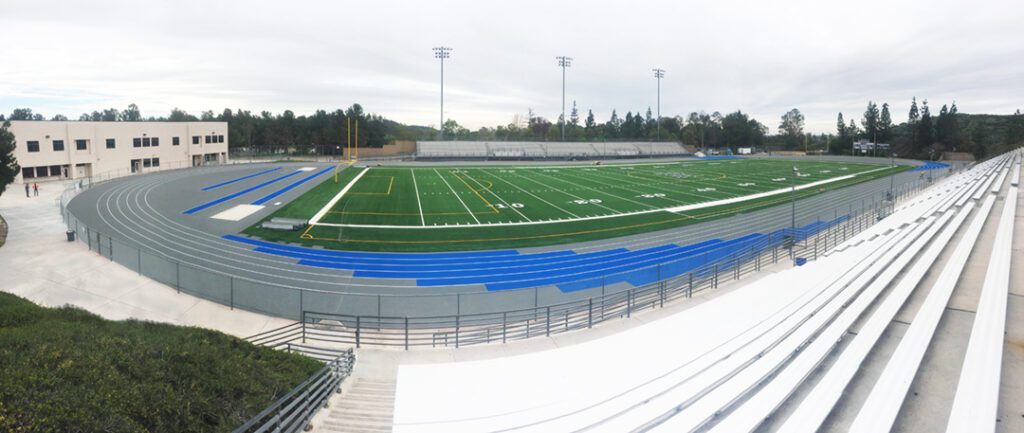 View of an empty football field with blue bleachers and goal posts.