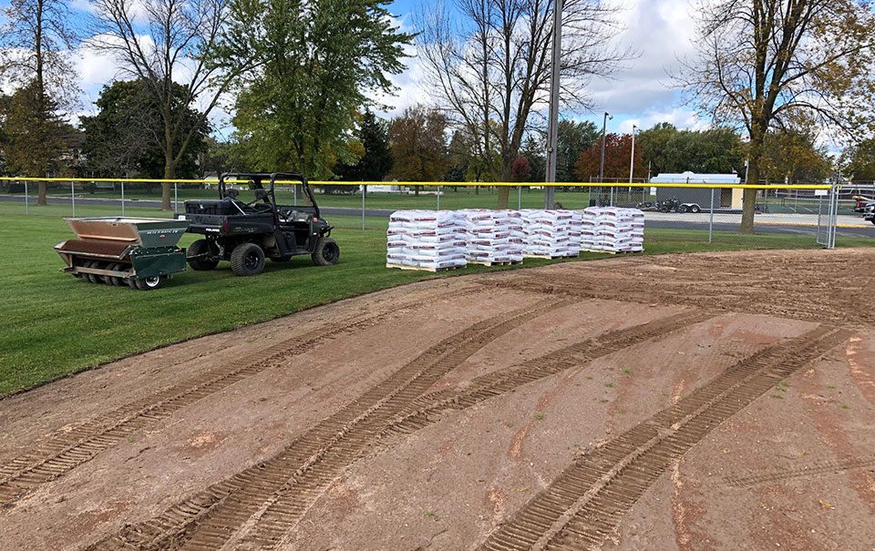 Golf carts and stacked bags near a dirt path on a grassy field.