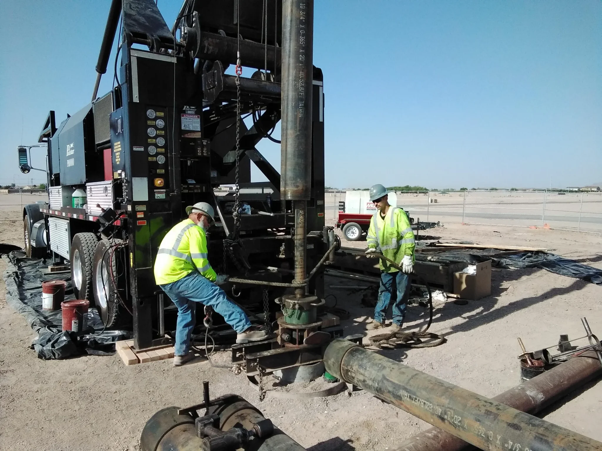 Workers operate heavy machinery on a construction site under clear skies.
