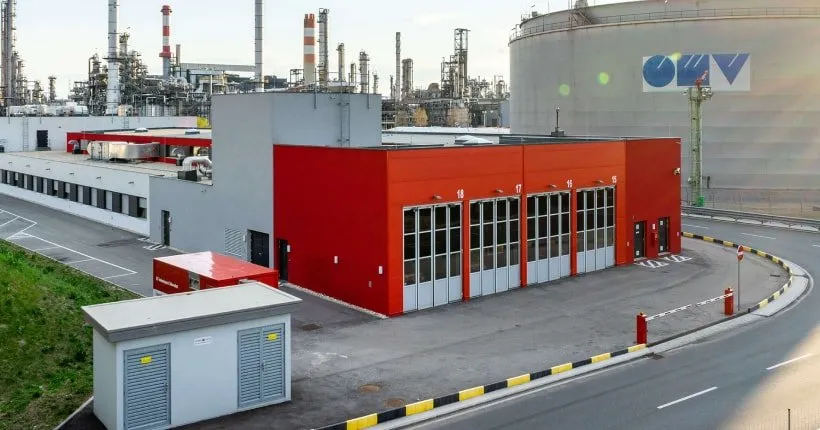 Red and white industrial building with multiple garage doors near a refinery.
