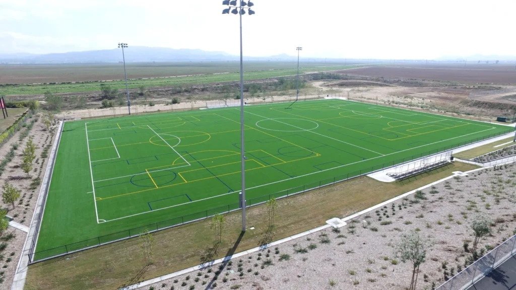 A large green sports field with marked lines under tall floodlights.