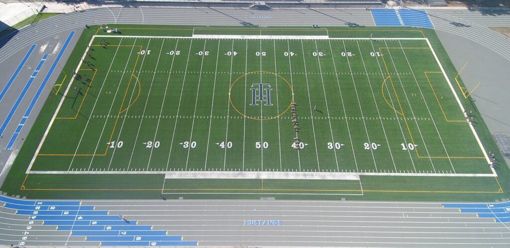 Aerial view of a football field with clear yard lines and a logo at the center.