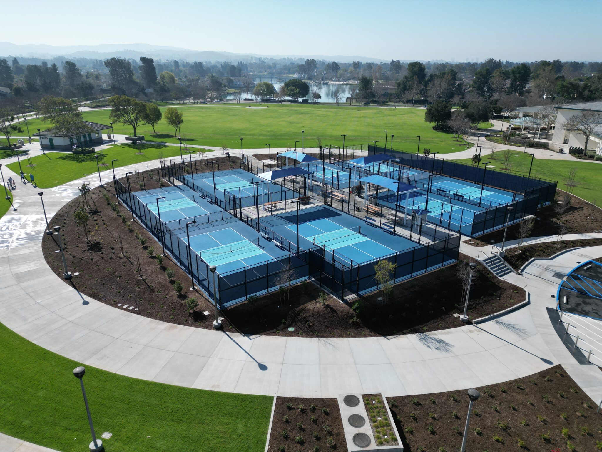 Aerial view of multiple blue pickleball courts in a fenced sports complex.
