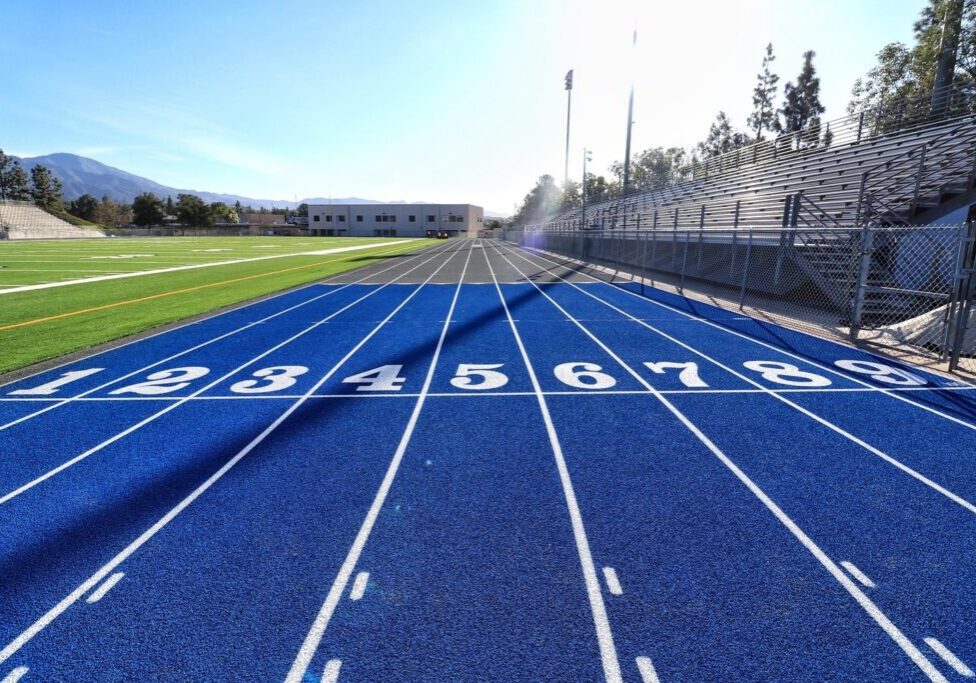 Blue running track lanes numbered 2 to 8 with a sports field in the background.