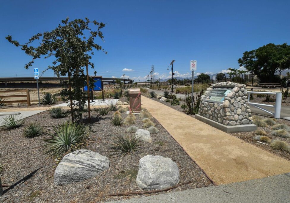 Sunny pathway through a landscaped park with stone features and a clear blue sky.