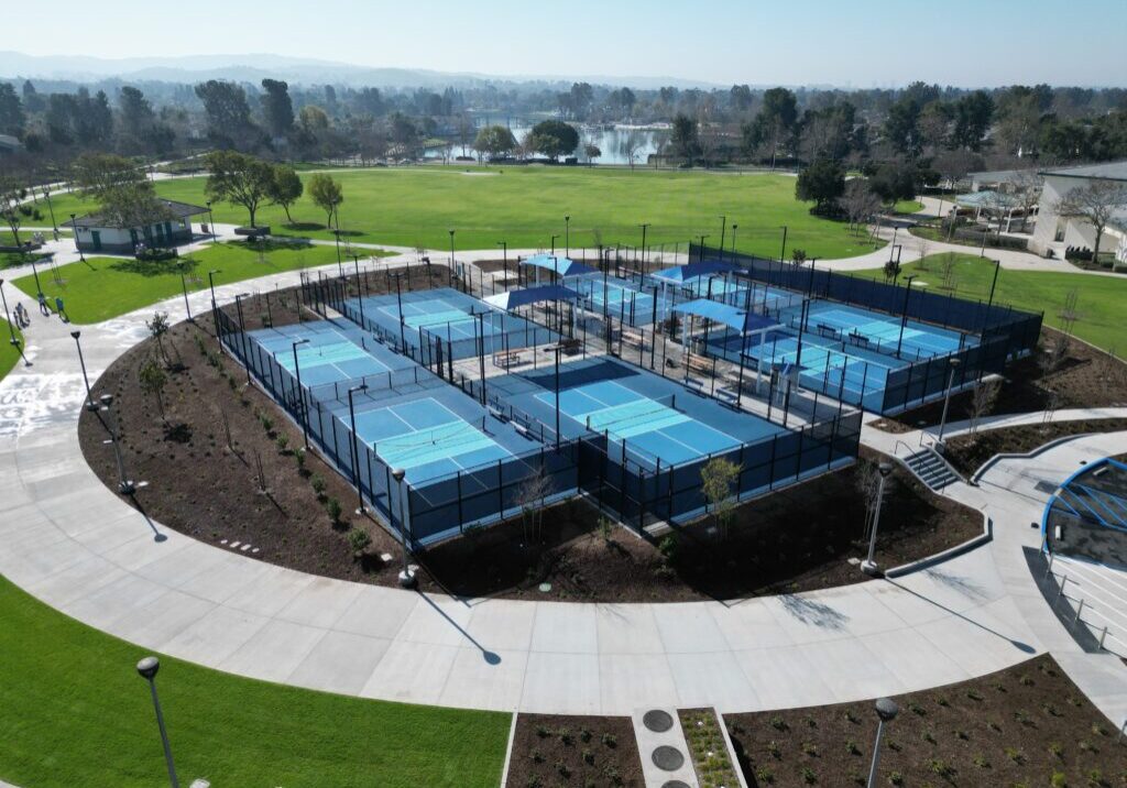 Aerial view of multiple blue pickleball courts in a fenced sports complex.