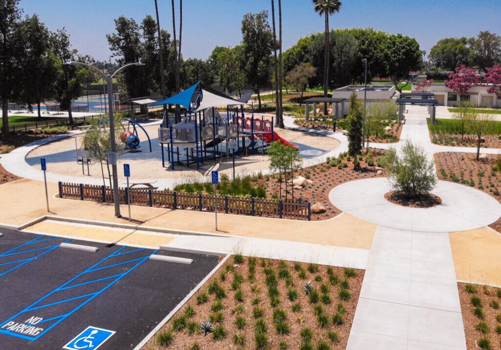 A sunny playground with slides and climbing structures near a parking lot.