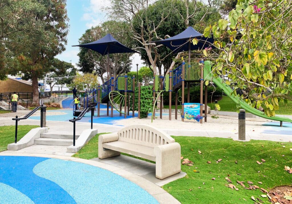 Modern playground with slides, swings, and benches in a park.
