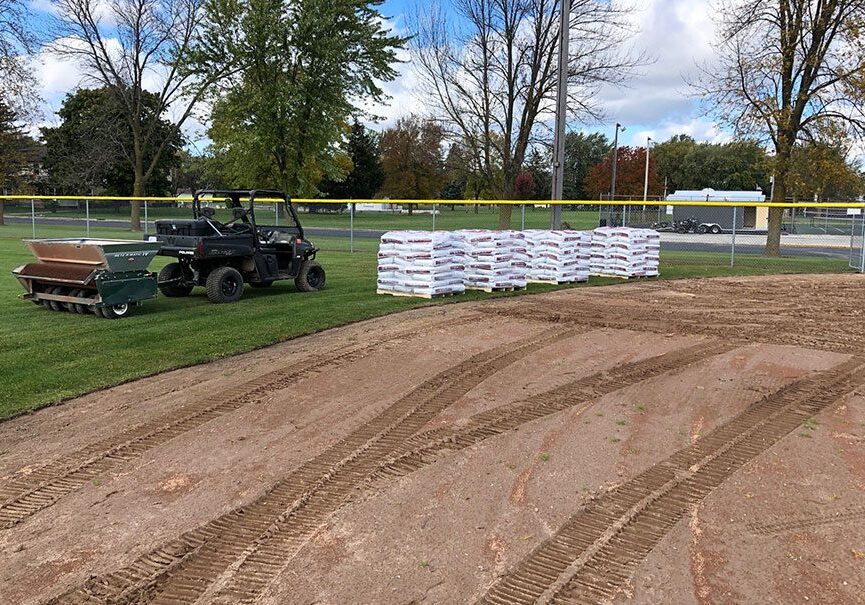Golf carts and stacked bags near a dirt path on a grassy field.