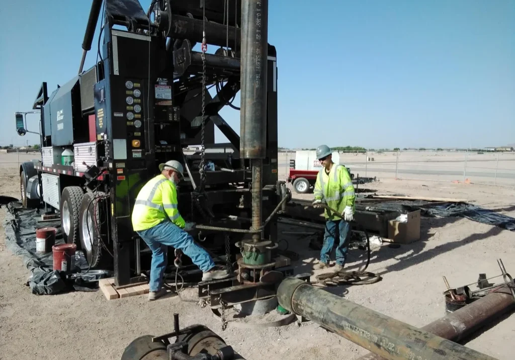 Workers operate heavy machinery on a construction site under clear skies.
