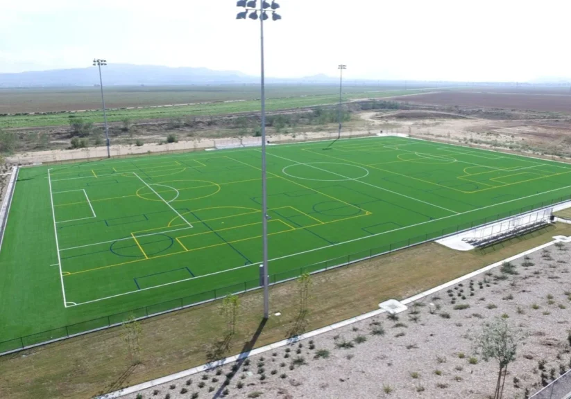 A large green sports field with marked lines under tall floodlights.